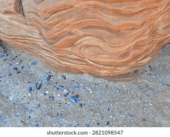 Dramatic red sandstone cliffs and exposed rock bed along the coastline of Hilbre Island at low tide under a bright blue sky, weathered red sandstone rock formations displaying natural erosion layers on the shore