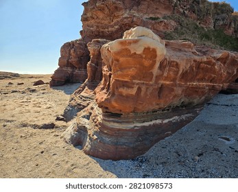 Dramatic red sandstone cliffs and exposed rock bed along the coastline of Hilbre Island at low tide under a bright blue sky, weathered red sandstone rock formations displaying natural erosion layers on the shore