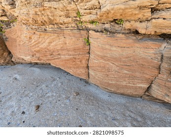 Dramatic red sandstone cliffs and exposed rock bed along the coastline of Hilbre Island at low tide under a bright blue sky, weathered red sandstone rock formations displaying natural erosion layers on the shore