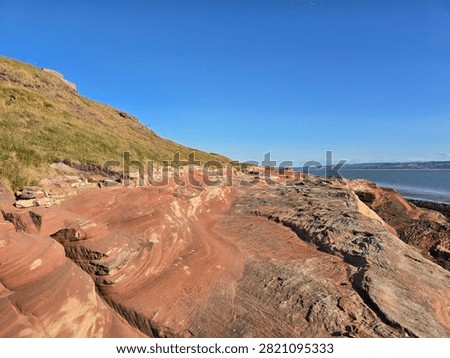 Dramatic red sandstone cliffs and exposed rock bed along the coastline of Hilbre Island at low tide under a bright blue sky, weathered red sandstone rock formations displaying natural erosion layers on the shore 