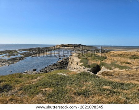 Dramatic red sandstone cliffs and exposed rock bed along the coastline of Hilbre Island at low tide under a bright blue sky, weathered red sandstone rock formations displaying natural erosion layers on the shore