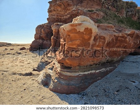 Dramatic red sandstone cliffs and exposed rock bed along the coastline of Hilbre Island at low tide under a bright blue sky, weathered red sandstone rock formations displaying natural erosion layers on the shore