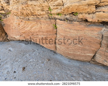 Dramatic red sandstone cliffs and exposed rock bed along the coastline of Hilbre Island at low tide under a bright blue sky, weathered red sandstone rock formations displaying natural erosion layers on the shore