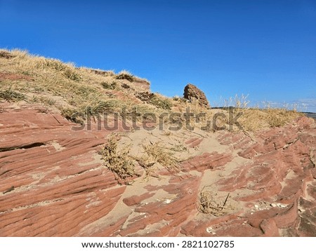 Dramatic red sandstone cliffs and exposed rock bed along the coastline of Hilbre Island at low tide under a bright blue sky, weathered red sandstone rock formations displaying natural erosion layers on the shore