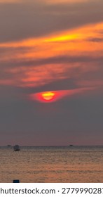 Dramatic red sun setting over a calm ocean horizon. Vibrant orange clouds create a stunning vertical seascape, perfect for nature and travel backgrounds.