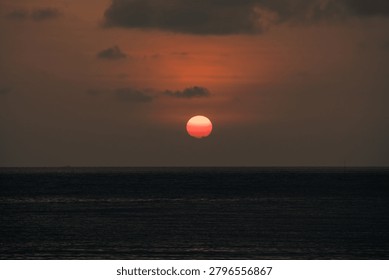 Dramatic red sunset with large sun disc sinking below the horizon over dark calm sea at Koh Samui Thailand