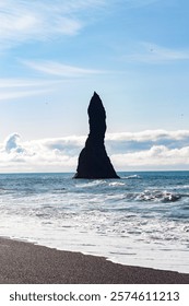 A dramatic rock formation rises from the ocean, surrounded by light waves and sunny skies.