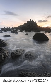 Dramatic rocky beach with misty waves and long exposure effect at sunset, natural seascape with soft pastel sky