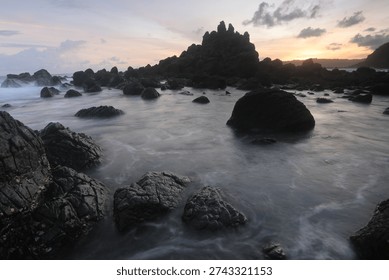 Dramatic rocky beach with misty waves and long exposure effect at sunset, natural seascape with soft pastel sky