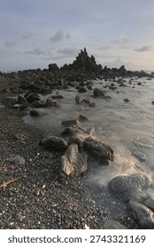 Dramatic rocky beach with misty waves and long exposure effect at sunset, natural seascape with soft pastel sky