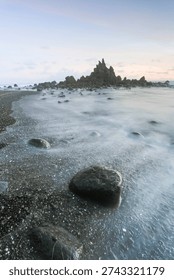 Dramatic rocky beach with misty waves and long exposure effect at sunset, natural seascape with soft pastel sky