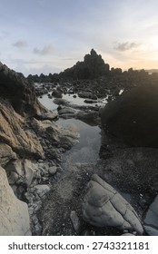 Dramatic rocky beach with misty waves and long exposure effect at sunset, natural seascape with soft pastel sky