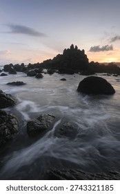 Dramatic rocky beach with misty waves and long exposure effect at sunset, natural seascape with soft pastel sky