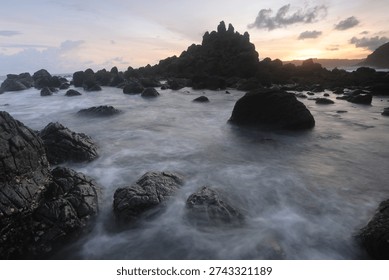 Dramatic rocky beach with misty waves and long exposure effect at sunset, natural seascape with soft pastel sky