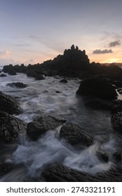 Dramatic rocky beach with misty waves and long exposure effect at sunset, natural seascape with soft pastel sky