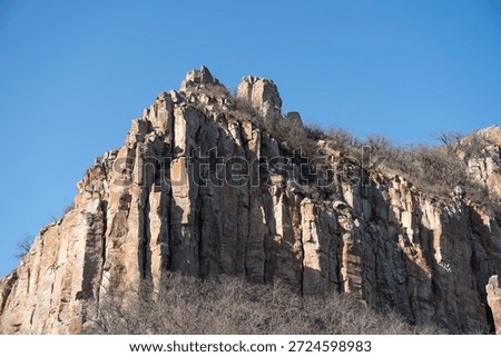 Dramatic rocky cliff rises against a clear blue sky in Armenia, vertical stone formations, warm earth tones, rugged mountain landscape