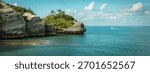 Dramatic rocky cliffs covered in lush green vegetation rise from the vibrant turquoise ocean under a partly cloudy sky.