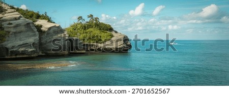 Dramatic rocky cliffs covered in lush green vegetation rise from the vibrant turquoise ocean under a partly cloudy sky.