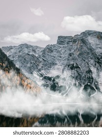 Dramatic rugged mountain cliffs partially covered in thick morning fog with a clear lake reflection