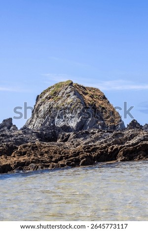 Dramatic rugged rocks frame a sandy beach and clear blue-green ocean under a bright sky. This wild coastal landscape evokes hidden coves and the untouched beauty of nature. Ideal for travel content