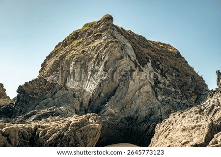 Dramatic rugged rocks frame a sandy beach and clear blue-green ocean under a bright sky. This wild coastal landscape evokes hidden coves and the untouched beauty of nature. Ideal for travel content