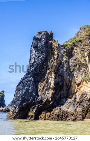 Dramatic rugged rocks frame a sandy beach and clear blue-green ocean under a bright sky. This wild coastal landscape evokes hidden coves and the untouched beauty of nature. Ideal for travel content