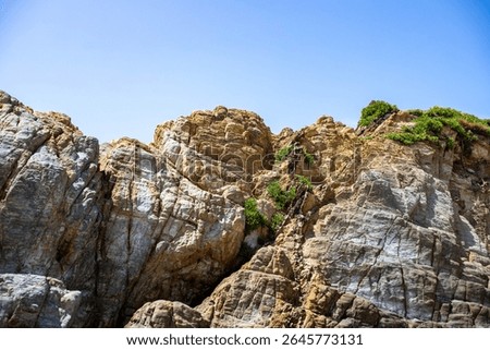 Dramatic rugged rocks frame a sandy beach and clear blue-green ocean under a bright sky. This wild coastal landscape evokes hidden coves and the untouched beauty of nature. Ideal for travel content