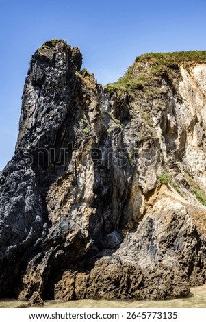 Dramatic rugged rocks frame a sandy beach and clear blue-green ocean under a bright sky. This wild coastal landscape evokes hidden coves and the untouched beauty of nature. Ideal for travel content