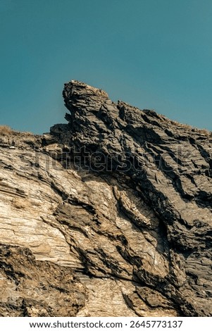 Dramatic rugged rocks frame a sandy beach and clear blue-green ocean under a bright sky. This wild coastal landscape evokes hidden coves and the untouched beauty of nature. Ideal for travel content