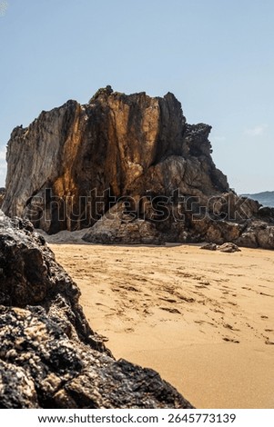 Dramatic rugged rocks frame a sandy beach and clear blue-green ocean under a bright sky. This wild coastal landscape evokes hidden coves and the untouched beauty of nature. Ideal for travel content
