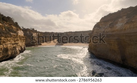 Dramatic sandstone cliffs surround a secluded sandy beach with rough ocean waves under soft light.