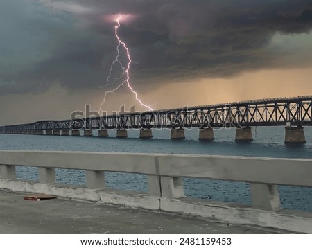 A dramatic scene of a lightning strike illuminating the sky over a historic bridge. The dark storm clouds and turbulent waters create a powerful and awe-inspiring moment captured in nature.
