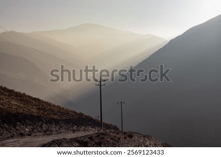 A dramatic scene of a mountain road with power lines silhouetted against a hazy sky.