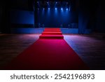 Dramatic scene with a red carpet staircase leading up to a stage, illuminated by blue spotlights. The stage is set for an award show, performance, or presentation.