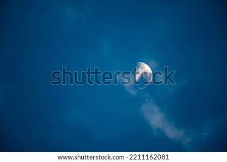 A dramatic scenery of the Moon behind the clouds in the blue sky at nigh