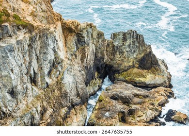 Dramatic sea cliffs at Devils Slide near Pacifica, California, featuring a rugged rock formation with a narrow ocean passage, waves crashing into the colorful layered stone.