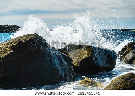 Dramatic sea spray erupts as a large wave hits the rugged, dark shoreline rocks near Anaga mountains