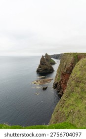 Dramatic sea stacks and high cliffs along the coastline under a cloudy sky.