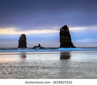 Dramatic sea stacks rising from the Pacific Ocean at Cannon Beach Oregon, USA, at sunset with colorful clouds reflected in the wet sand. Serene coastal landscape featuring ocean waves, rocky shoreline, and tranquil pastel skies