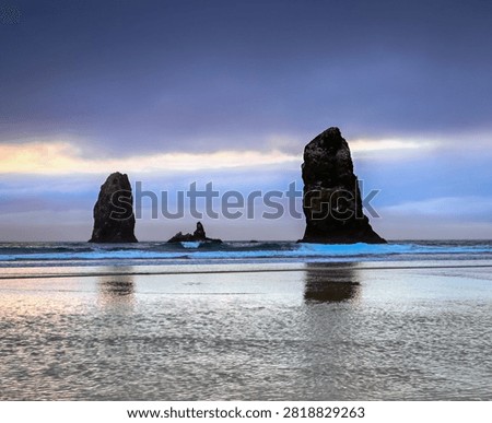 Dramatic sea stacks rising from the Pacific Ocean at Cannon Beach Oregon, USA, at sunset with colorful clouds reflected in the wet sand. Serene coastal landscape featuring ocean waves, rocky shoreline, and tranquil pastel skies