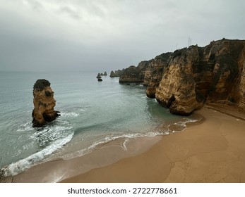 Dramatic sea stacks and sandy beach under the overcast sky in Lagos, Faro, Algarve, Portugal, February 2025