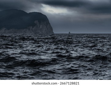 Dramatic seascape before a storm, view of the dark sea with waves, and silhouettes of high cliffs and clouds in the distance