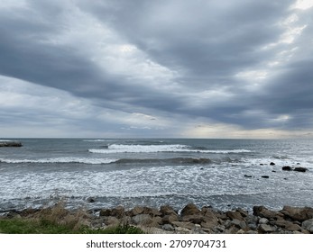 Dramatic seascape features rolling waves crashing on rocky shore, with a moody sky overhead, evoking a sense of calm and natural beauty