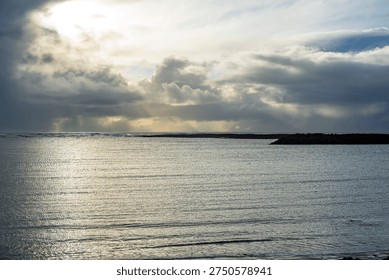 Dramatic seascape with sunlight breaking through dark storm clouds over calm ocean water