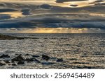 A dramatic seascape at sunset with dark clouds and sunlight over the ocean.