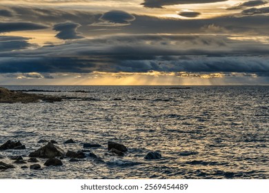 A dramatic seascape at sunset with dark clouds and sunlight over the ocean.
