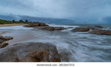 Dramatic seascape at twilight with ocean waves crashing against dark rocky shoreline under cloudy sky
