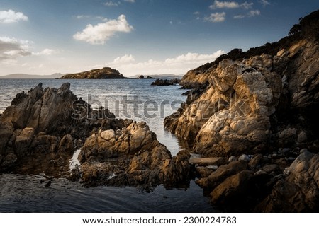 Dramatic seascape view during sunset in Costa Smeralda, Sardinia. The photo showcases the contrast between the calm, sparkling sea and the rugged rocks that dominate the scene