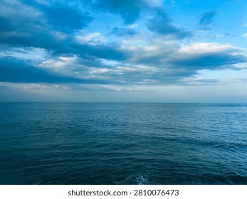 Dramatic Seaside View with Dark Rocks and Ocean Waves.  A powerful coastal scene showing waves flowing toward a rocky shoreline beneath a cloudy sky. This image captures the raw beauty of nature and is suitable for travel, ocean, weather, and environmental themes.