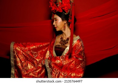 Dramatic Series Female Express Feeling Emotional With Fabric Fluttering In The Air. Asian Woman Wear China Royal Empress Traditional Costume With Golden Line Design Dress And Headwear, Red Background